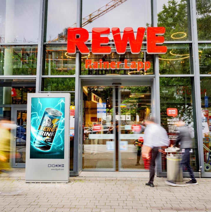 Gläserne Werbevitrine mit Werbung für Energie vor Rewe-Markt